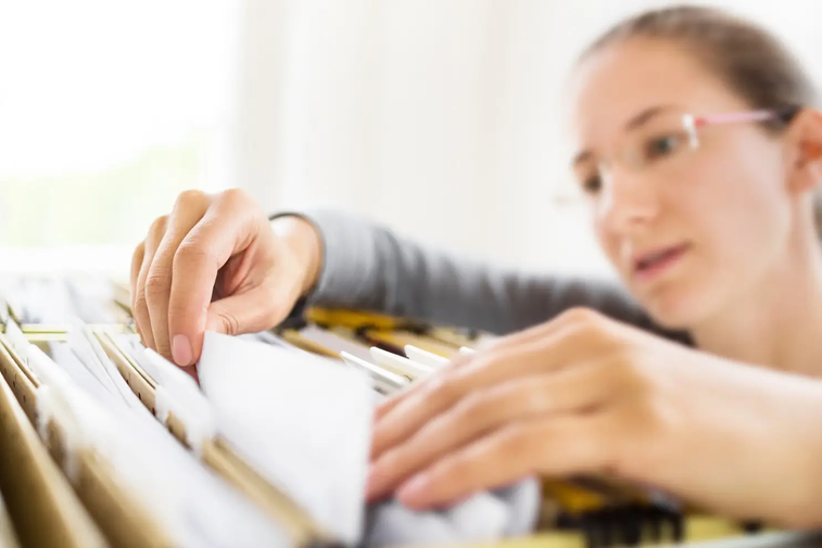 Woman searching through files in metal file cabinet